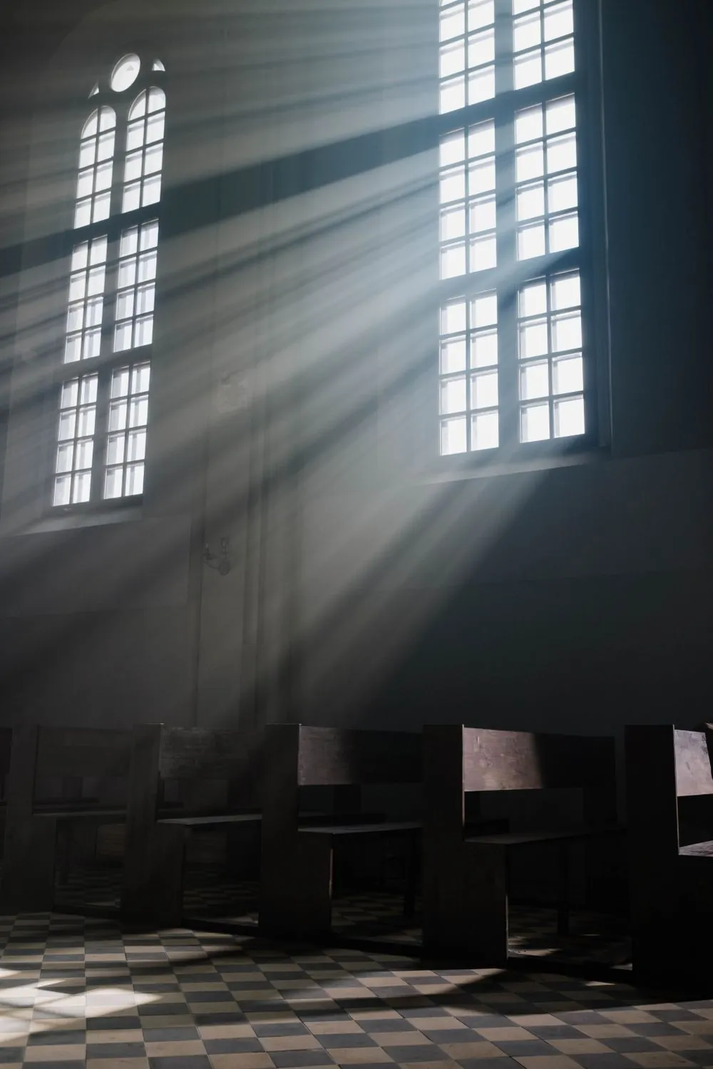 Sunlight streaming through tall church windows over wooden pews