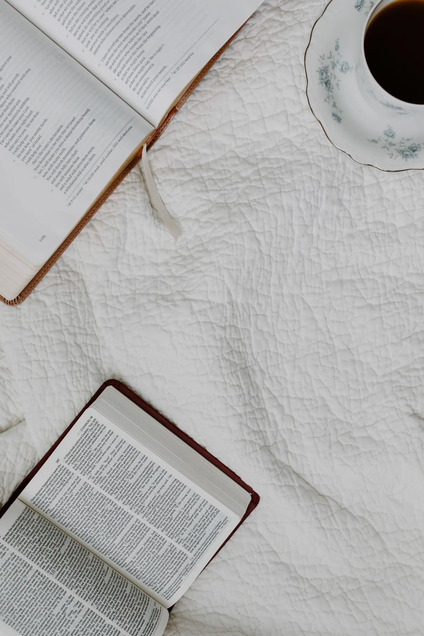 Open books and a cup of coffee on a white coverlet