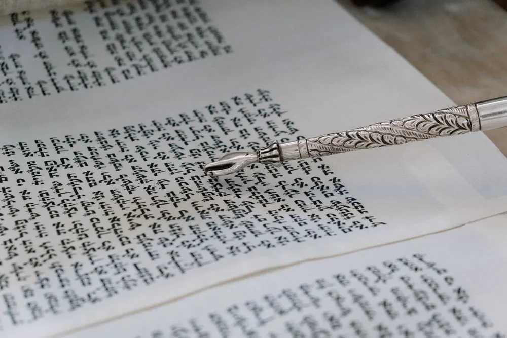A silver pointer resting on the Hebrew text of a Torah scroll
